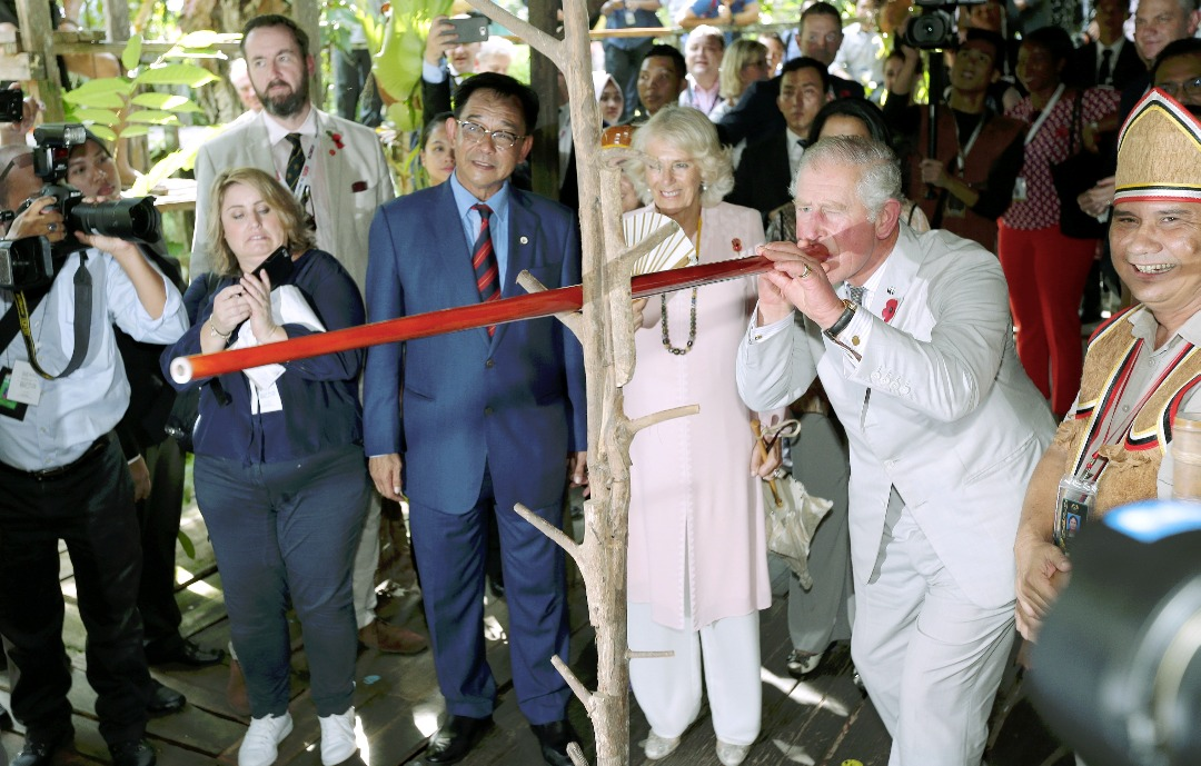 Image shows Prince Charles firing a dart from a blowpipe, on his left Camilla and Abdul Karim.